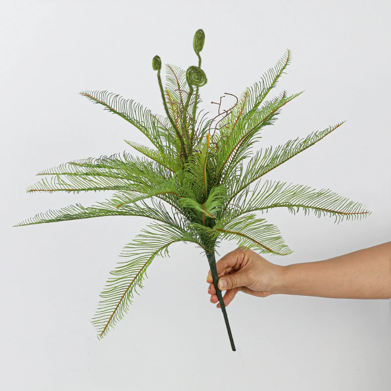 With unfurling fiddleheads artificial fern bush with coiled fiddleheads left unopened among the fronds, held in one hand