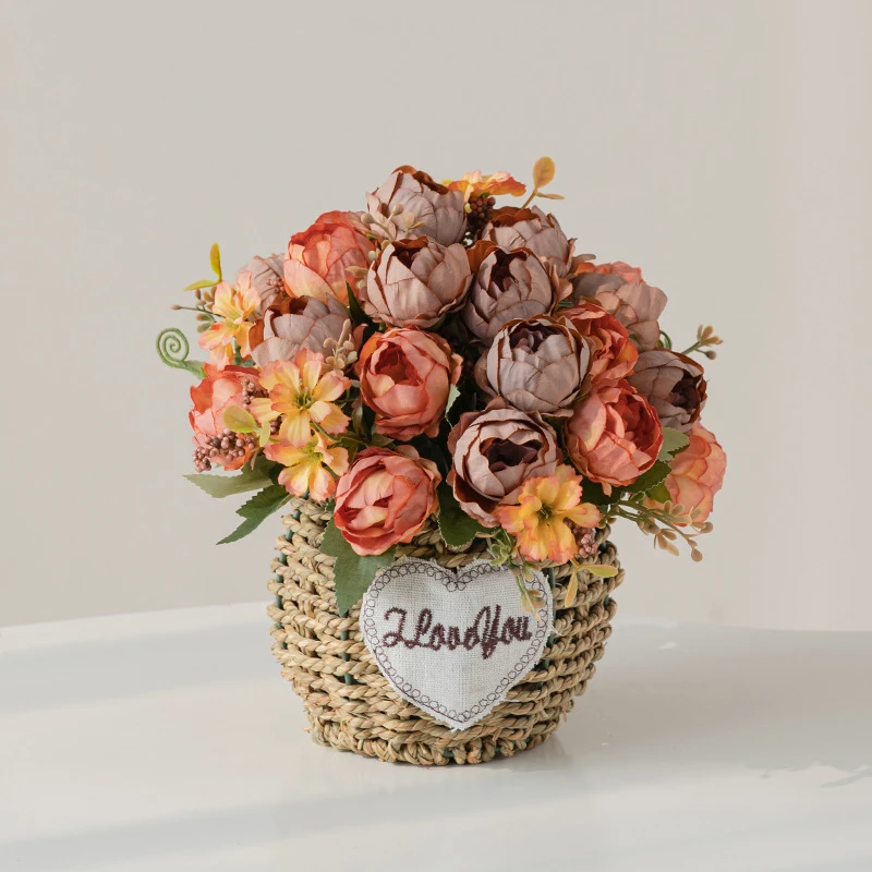 Coral peony artificial flower gift basket in a round woven basket with a heart-shaped tag, styled on a table top