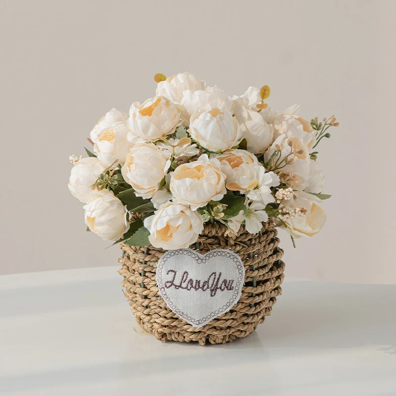 Ivory peony artificial flower gift basket in a round woven basket with a heart-shaped tag, styled on a table top