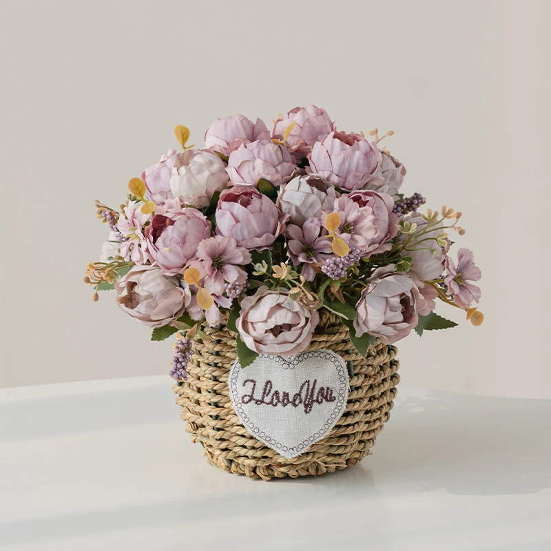 Lilac peony artificial flower gift basket in a round woven basket with a heart-shaped tag, styled on a table top