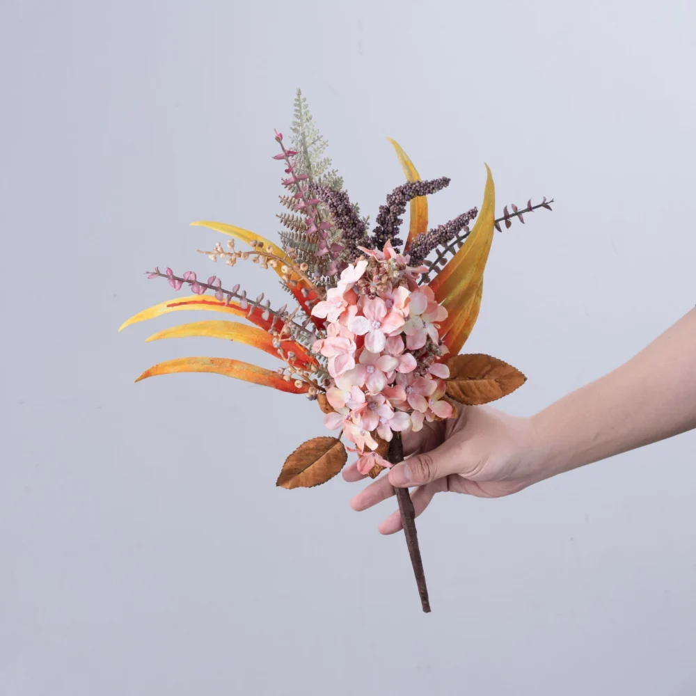 Coral, held artificial hydrangea pick built round one hydrangea head with autumn foliage behind it, held in one hand