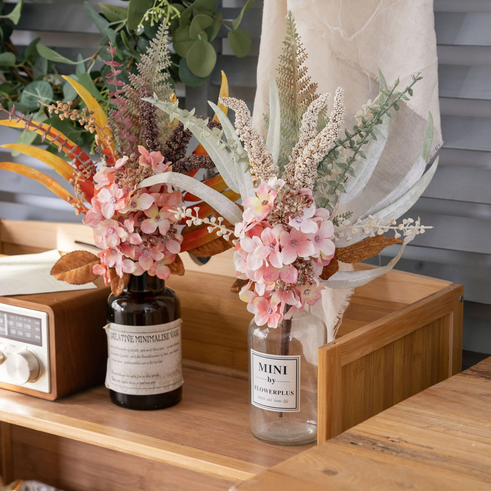 Two in bottle vases artificial hydrangea pick built round one hydrangea head with autumn foliage behind it, styled in a room setting