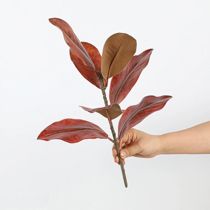 Red and bronze artificial magnolia leaf branch with the suede brown reverse left on every leaf, held in one hand