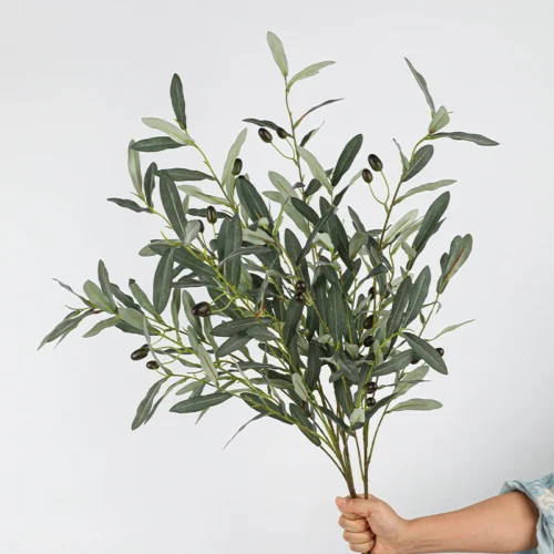 Grey green, held artificial olive branch with fruit carrying green and black olives along the stem, held in one hand