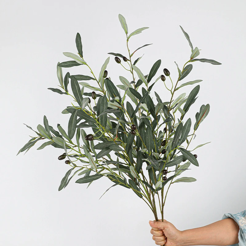 Grey green, held artificial olive branch with fruit carrying green and black olives along the stem, held in one hand