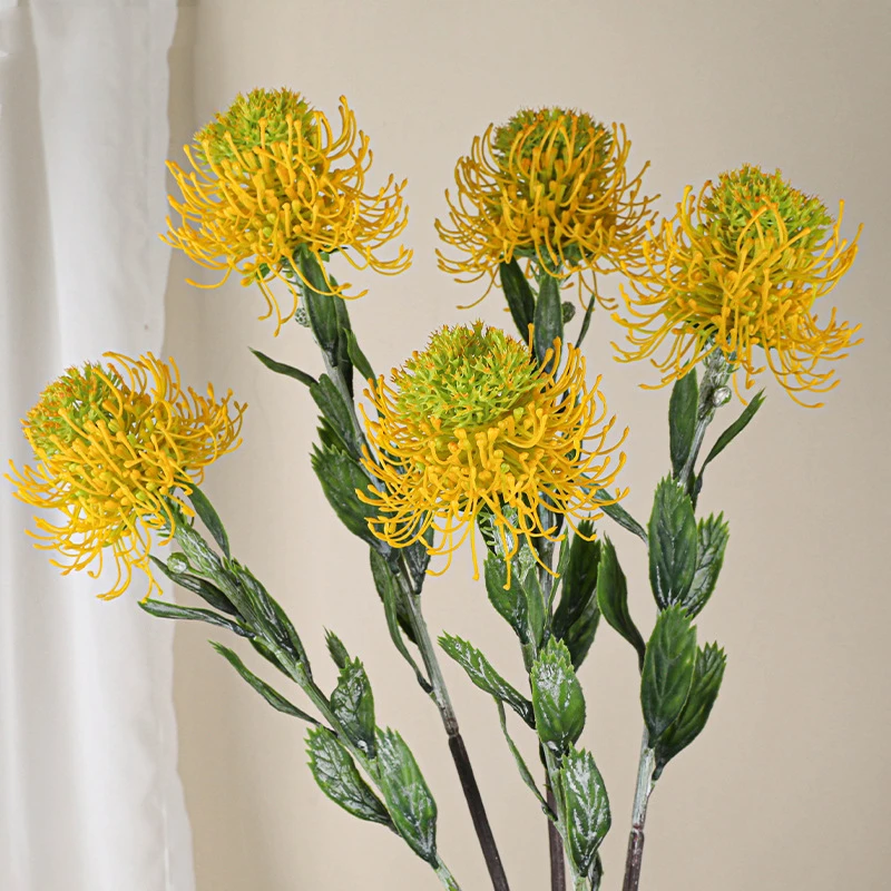 Yellow trio artificial pincushion protea stem with a head of radiating needle petals, styled on a table top