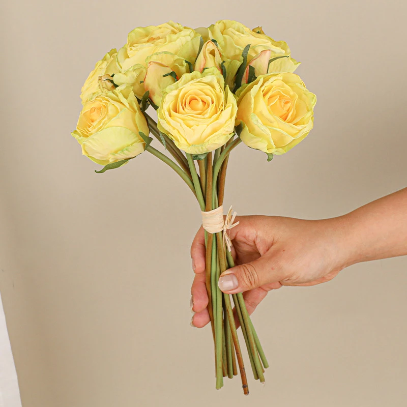 Yellow, held artificial rose posy of twelve roses tied at the stem with raffia, held in one hand