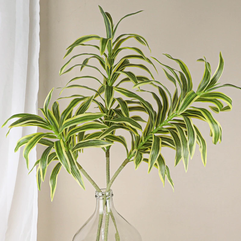 In a glass vase artificial spider plant stem with long arching variegated straps, arranged in a vase