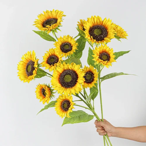 A bunch, held upright artificial sunflower stem carrying three heads at different stages on one long stem, held in one hand