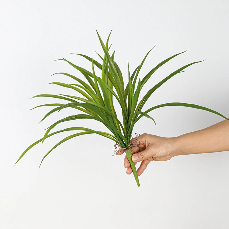 Held artificial tall grass plant as a dense tuft of long narrow blades, held in one hand