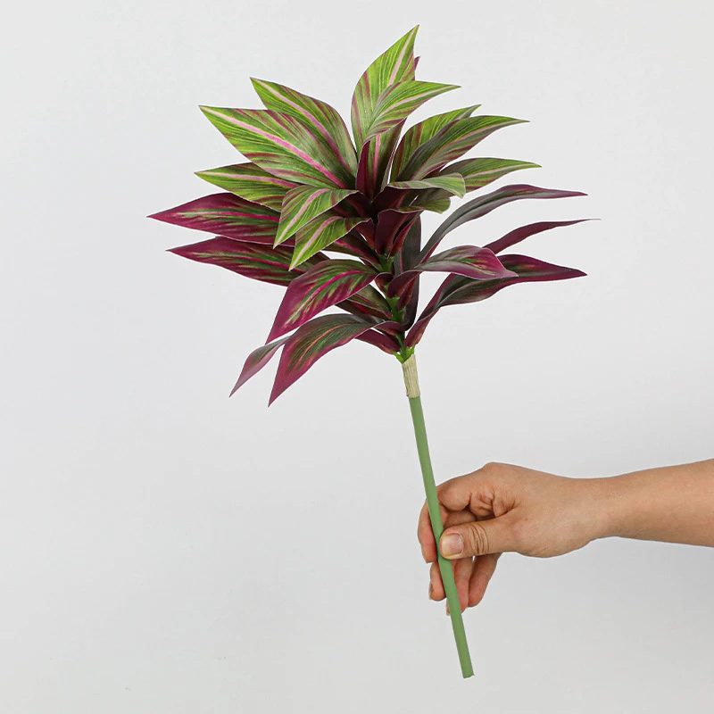 Burgundy tuft artificial tropical leaf bush of patterned leaves gathered on one short stalk, held in one hand