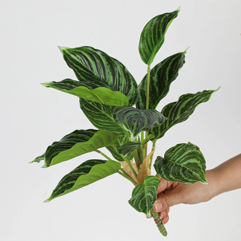 Dark green striped artificial tropical leaf bush of patterned leaves gathered on one short stalk, held in one hand