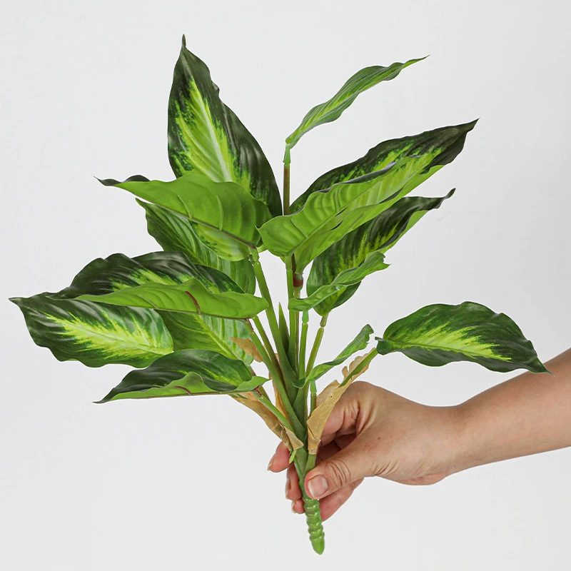 Green and cream artificial tropical leaf bush of patterned leaves gathered on one short stalk, held in one hand