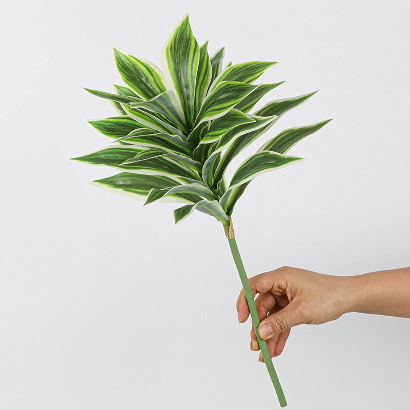 Green and cream tuft artificial tropical leaf bush of patterned leaves gathered on one short stalk, held in one hand