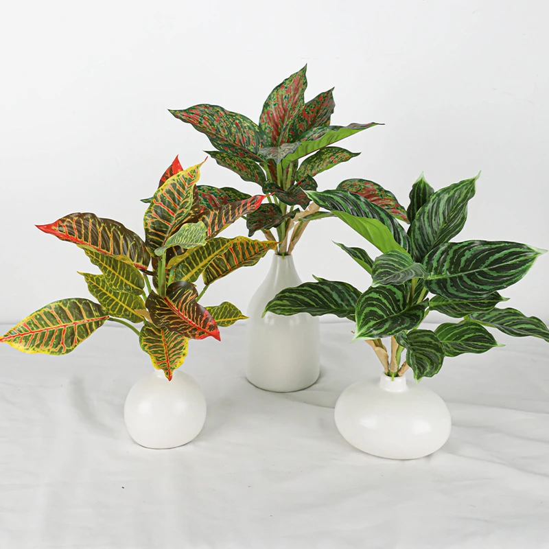 Three in white vases artificial tropical leaf bush of patterned leaves gathered on one short stalk, styled on a table top