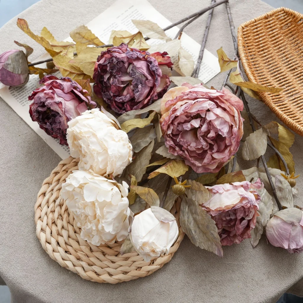 The full range, on a mat dried look artificial peony stem carrying three blooms and a bud on one stem, styled on a table top