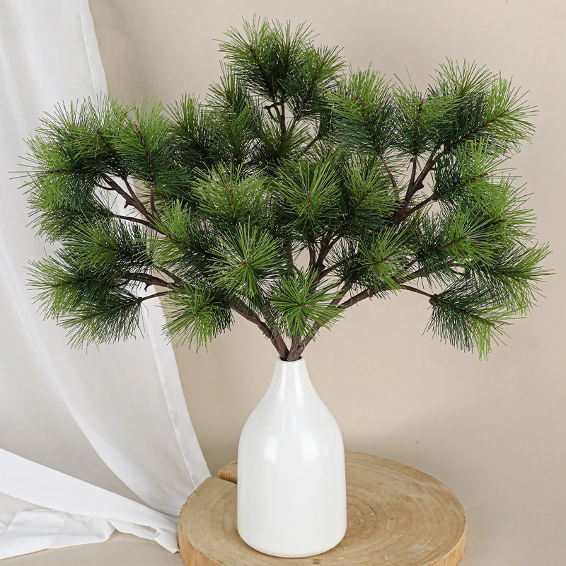 In a white vase fake pine branch with long soft needles on a bendable stem, arranged in a vase